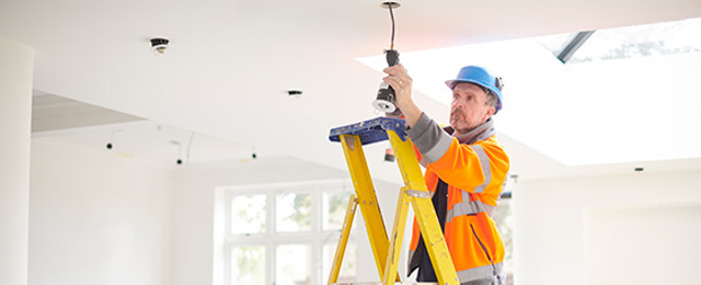 Electrician on a ladder working on a spotlight in a home being renovated