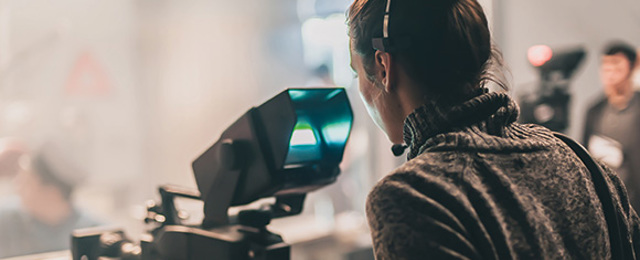 Woman behind a TV camera filming with a blurred background