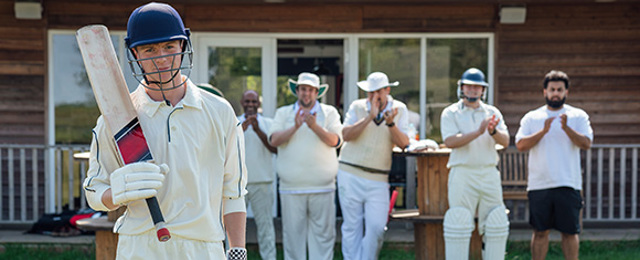 Cricketers lined up clapping a player outside a clubhouse