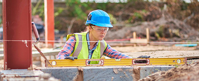 Women wearing hard hat using spirit level on breeze blocks in a building site