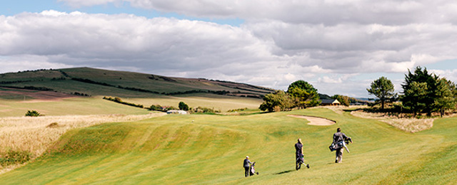 Three golfers carrying their clubs across a golf course