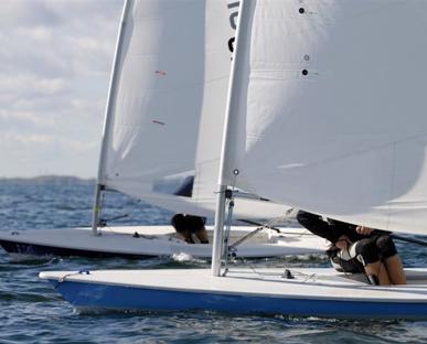 Two sailing boats at sea on a sunny day with the legs of the sailors visible