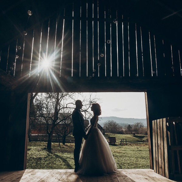Silhouette of a bride and groom face to face in a barn with sunlight streaming through