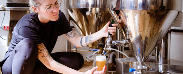 Women Crouching Pouring A Pint From A Brewing Tank