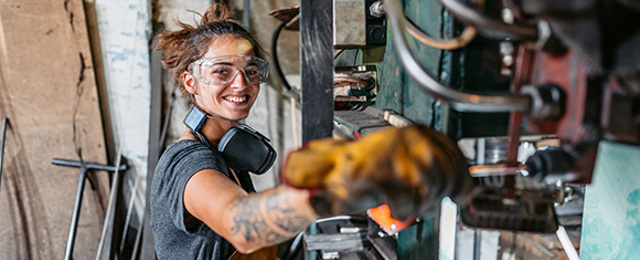 Woman with ear defenders and safety goggles working an industrial machine