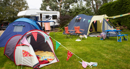 3 colourful tents with bunting outside on green grass with a caravan in the background